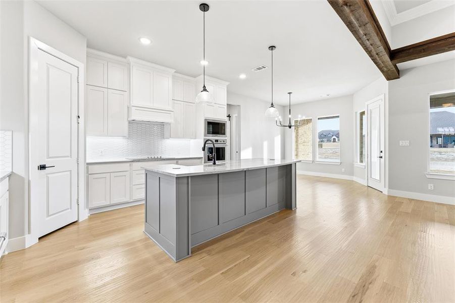 Kitchen with white cabinets, decorative light fixtures, light stone countertops, light wood-style floors, and recessed lighting
