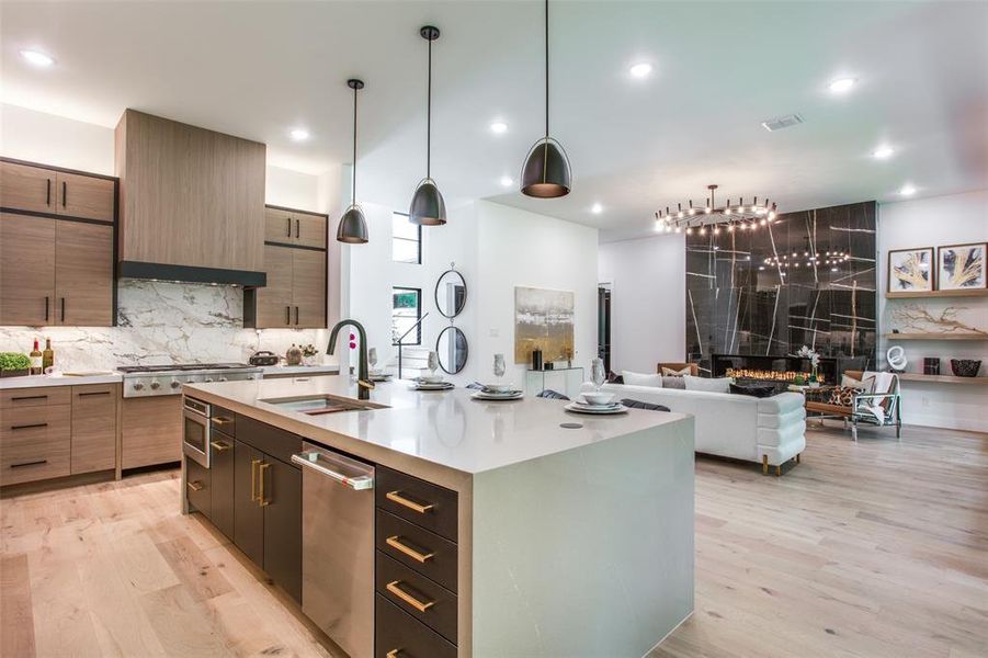 Kitchen featuring sink, stainless steel appliances, hanging light fixtures, an island with sink, and light hardwood / wood-style floors