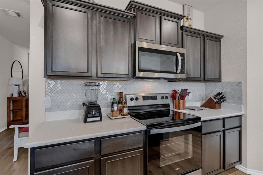 Kitchen featuring tasteful backsplash, appliances with stainless steel finishes, light wood finished floors, and visible vents