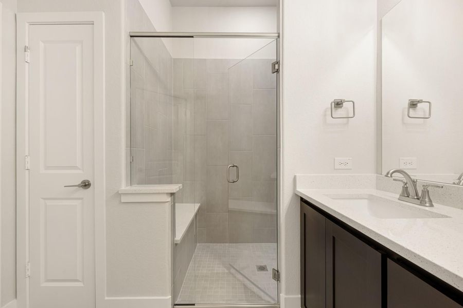 Bathroom with glass-enclosed tile shower, built-in bench, and dark vanity with white quartz countertop
