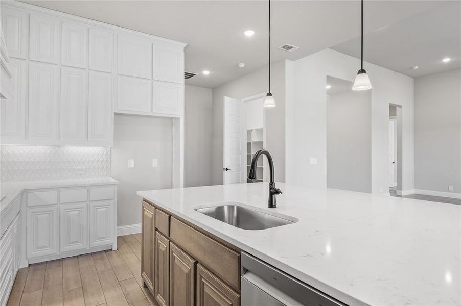 Kitchen featuring white cabinetry, light stone counters, decorative light fixtures, light wood-style floors, and dishwasher