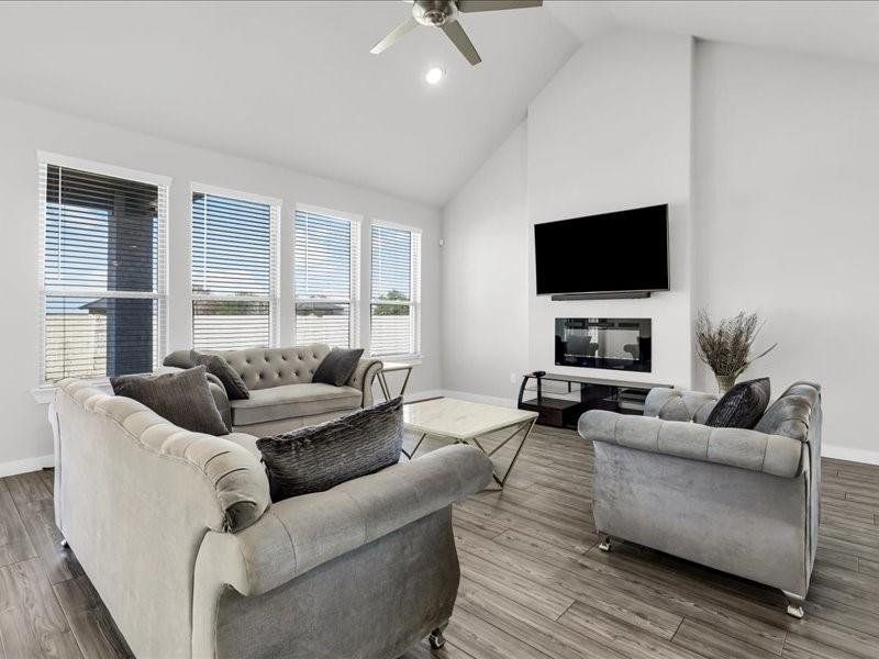 Living room with ceiling fan, high vaulted ceiling, and wood-type flooring