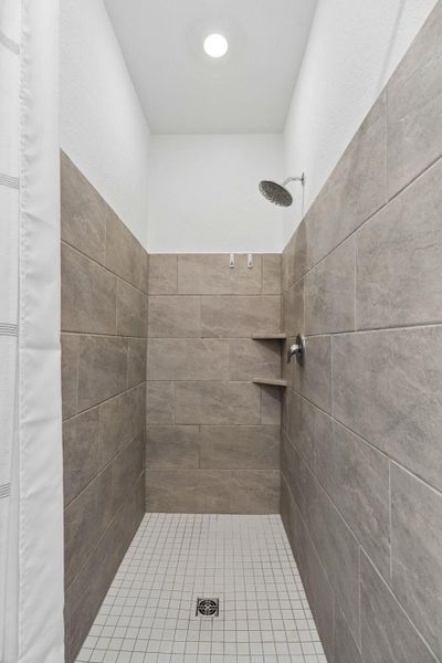 A well-lit shower features sleek tiled walls and a functional shower head in the primary bathroom