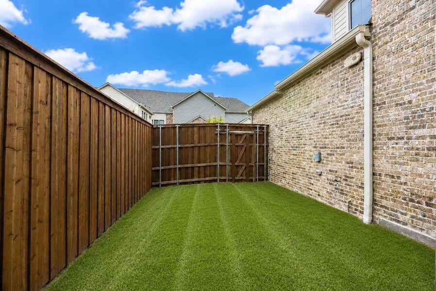 Private side yard featuring a lush green lawn, full privacy fencing, and a brick exterior wall with integrated downspout