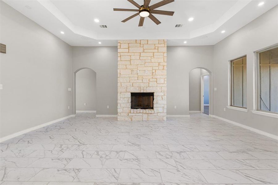 Unfurnished living room featuring arched walkways, a ceiling fan, a fireplace, a tray ceiling, and recessed lighting