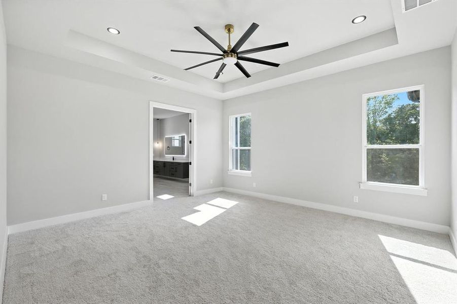 Unfurnished room with a tray ceiling, light colored carpet, and ceiling fan Unfurnished room with a tray ceiling, light colored carpet, and ceiling fan