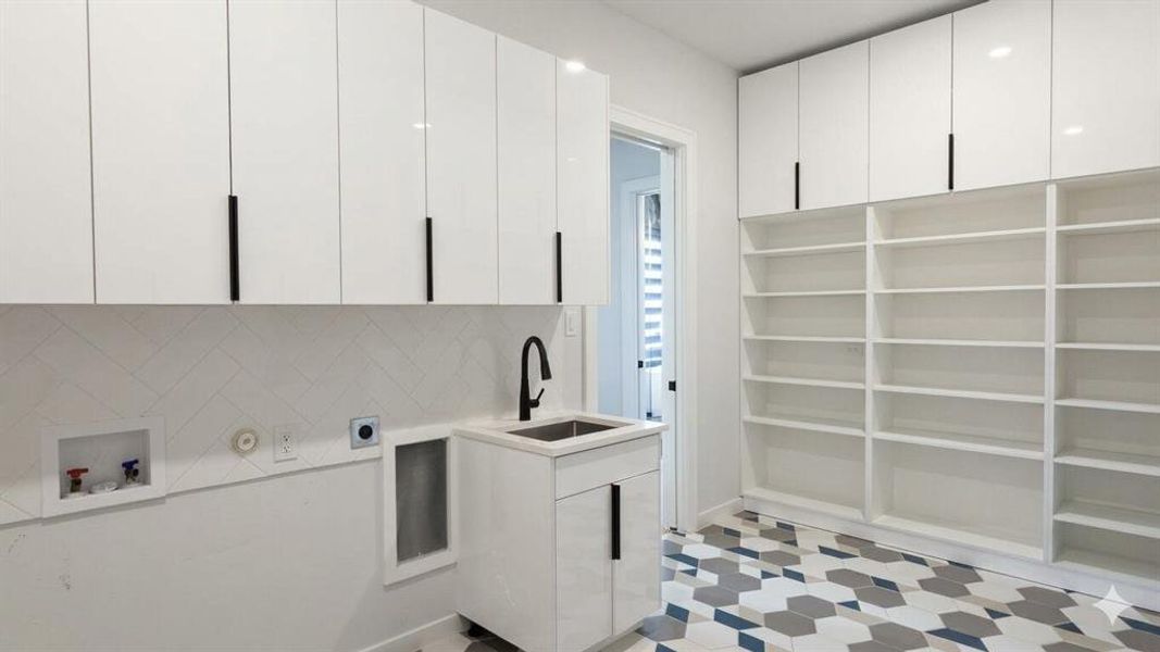 Modern laundry room featuring a utility sink, matte black faucet, and ample built-in cabinetry with black hardware