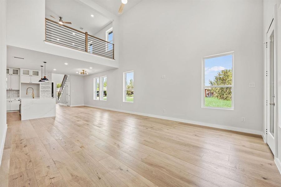 Unfurnished living room with beam ceiling, light hardwood / wood-style flooring, a wealth of natural light, and a high ceiling