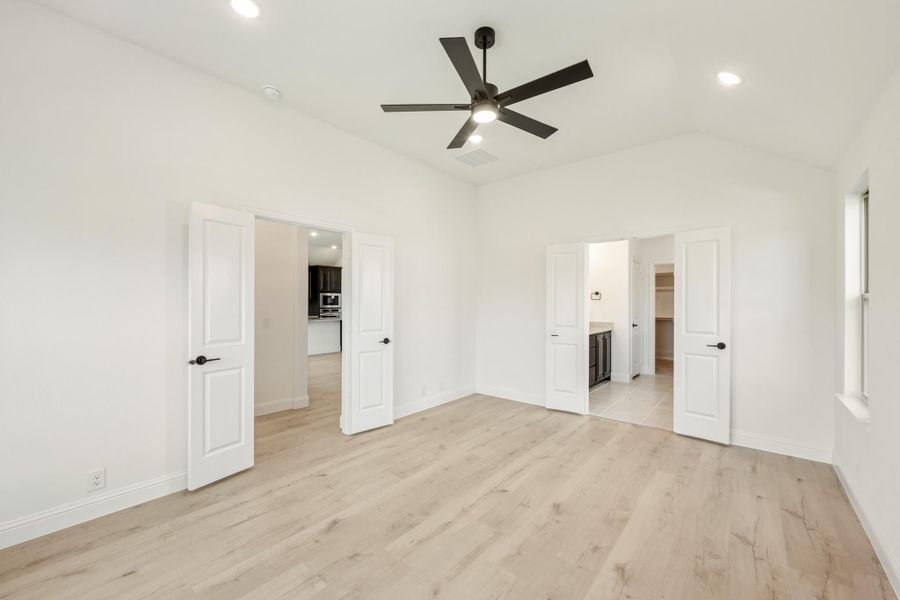 Empty master bedroom with light wood floors, black ceiling fan, and doors leading to bathroom and closet