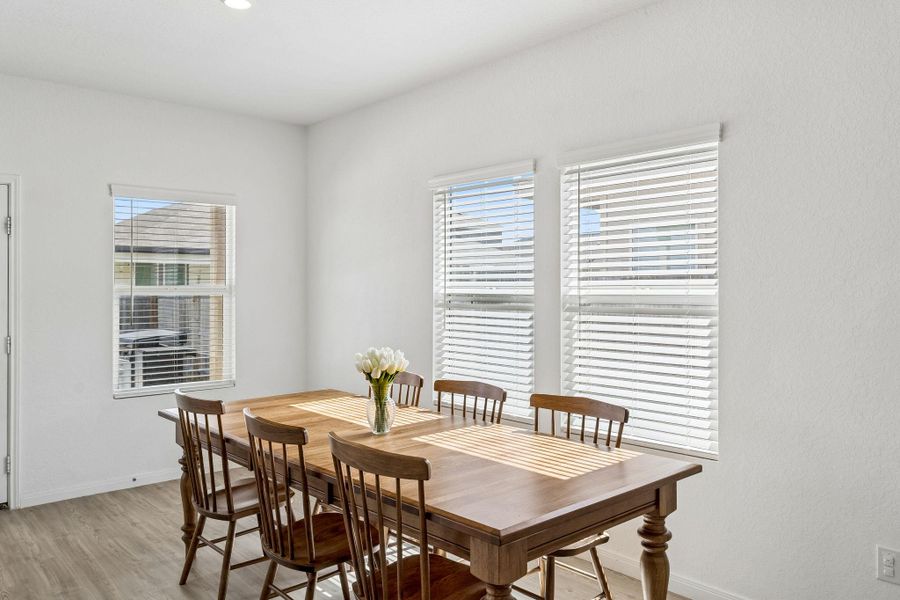 Sunlight streams into this dining space, highlighting the LVP flooring and clean lines of the walls.