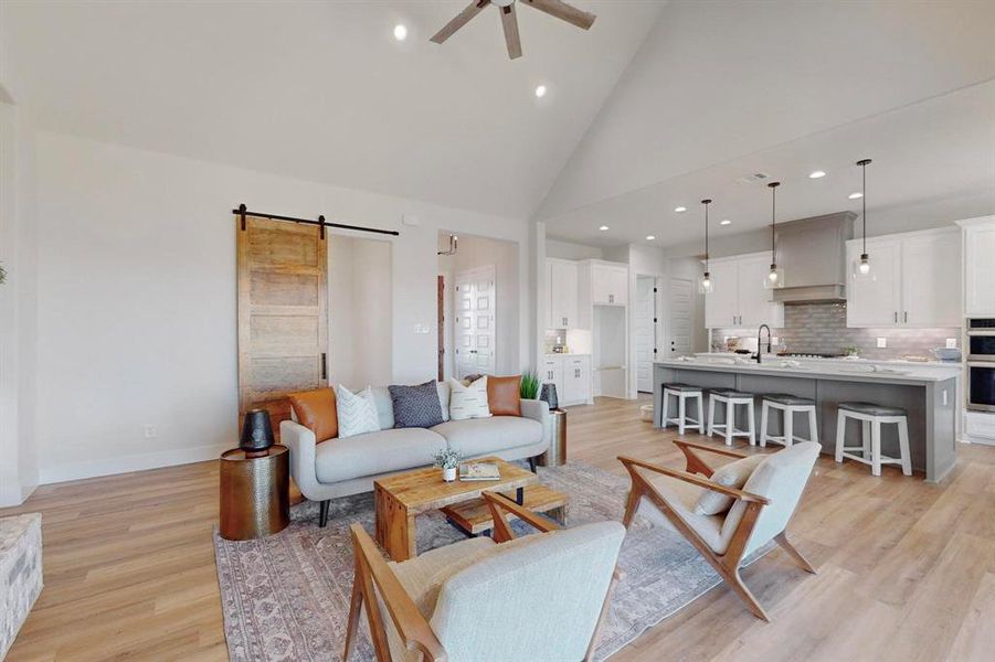 Living room featuring sink, a barn door, high vaulted ceiling, and light hardwood / wood-style flooring