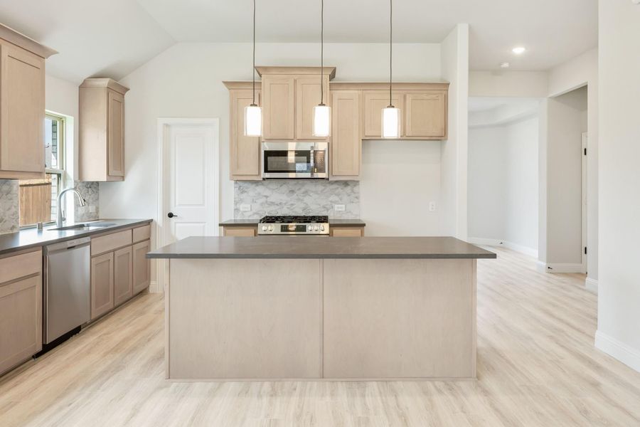 Kitchen with light wood cabinets, center island, stainless steel appliances, and pendant lights over light hardwood floors