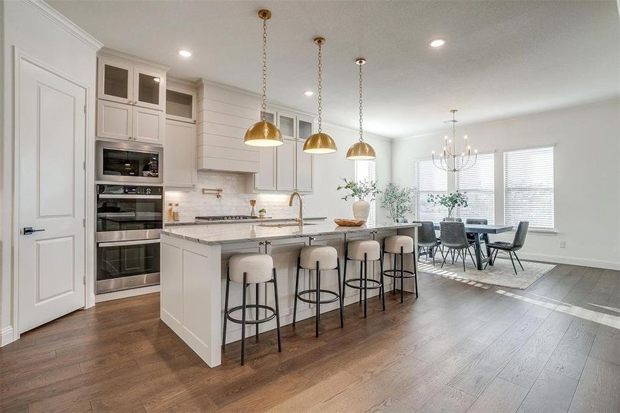 Kitchen featuring a large island, Quartzite countertops, gold hardware, decorative light fixtures, custom cabinetry to the ceiling, gas cooktop, double oven and walk in pantry