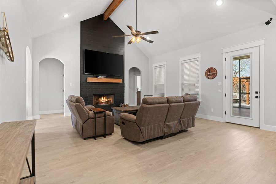 Living room featuring beamed ceiling, ceiling fan, a fireplace, high vaulted ceiling, and light hardwood / wood-style flooring