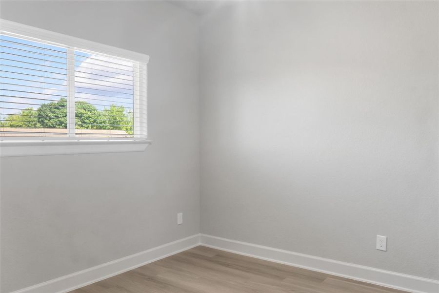 This photo shows a small, bright room with light-colored walls and flooring. It features a window with blinds, offering a view of greenery outside. Ideal for a cozy office or guest room.