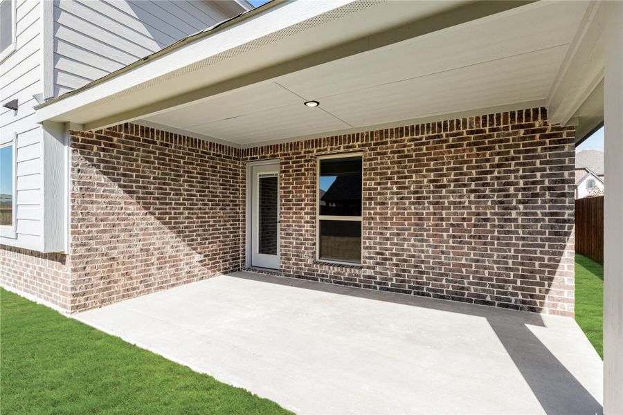 Covered back patio with concrete slab, brick exterior wall, and back door entry with green lawn