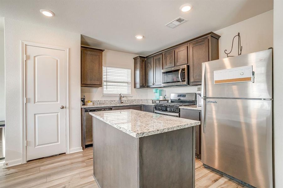 Kitchen featuring appliances with stainless steel finishes, light stone counters, a center island, light wood-style floors, and dark brown cabinets