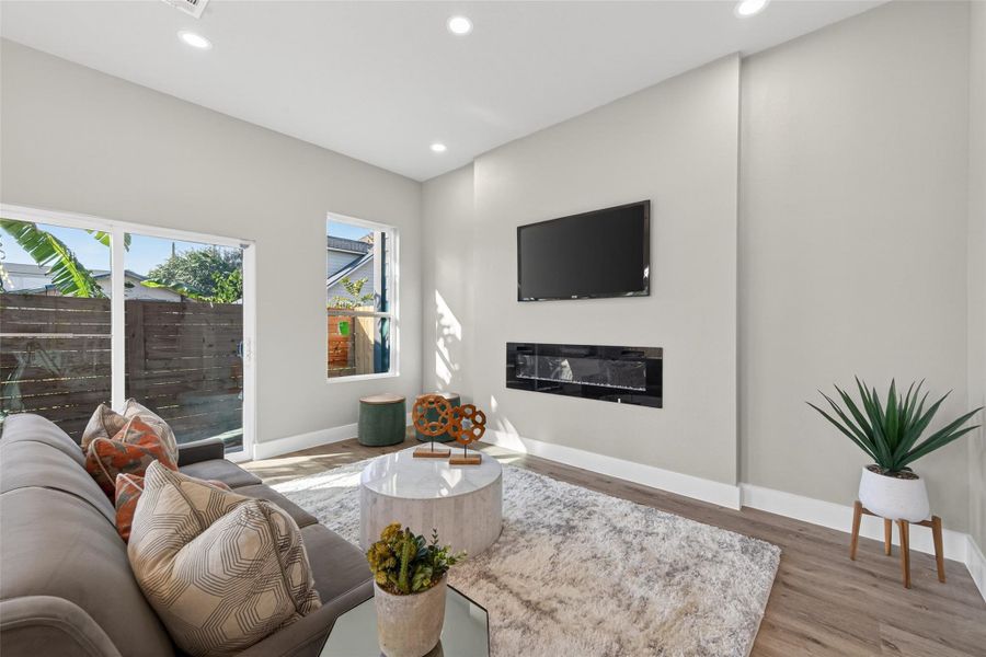 Spacious living room featuring a sleek wall-mounted electric fireplace, recessed lighting, and an open layout designed for comfort, entertaining, and modern living.