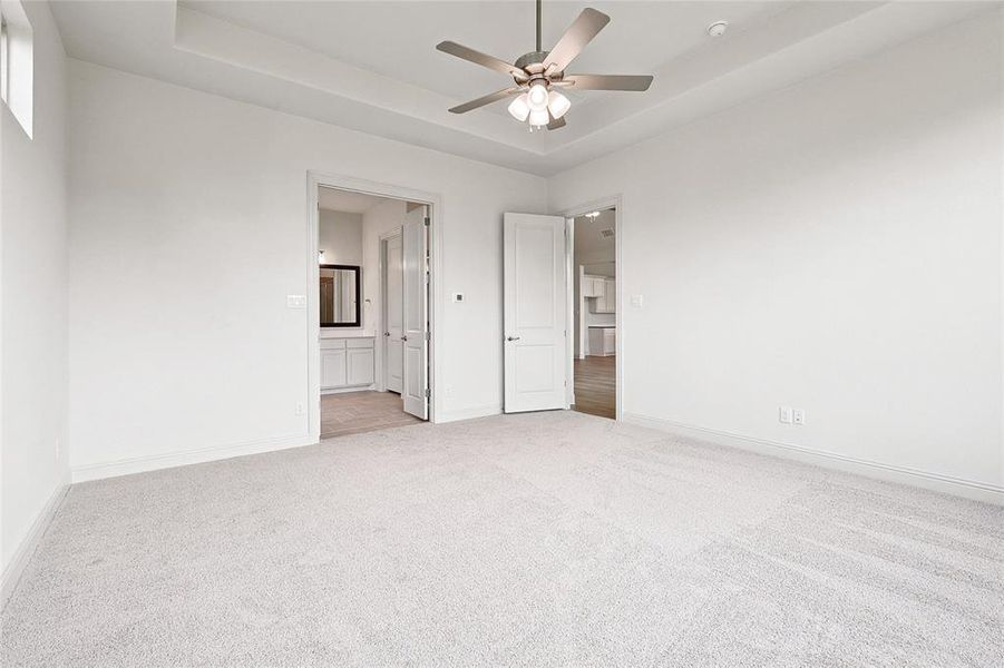 Unfurnished bedroom featuring ensuite bathroom, carpet, ceiling fan, and a tray ceiling