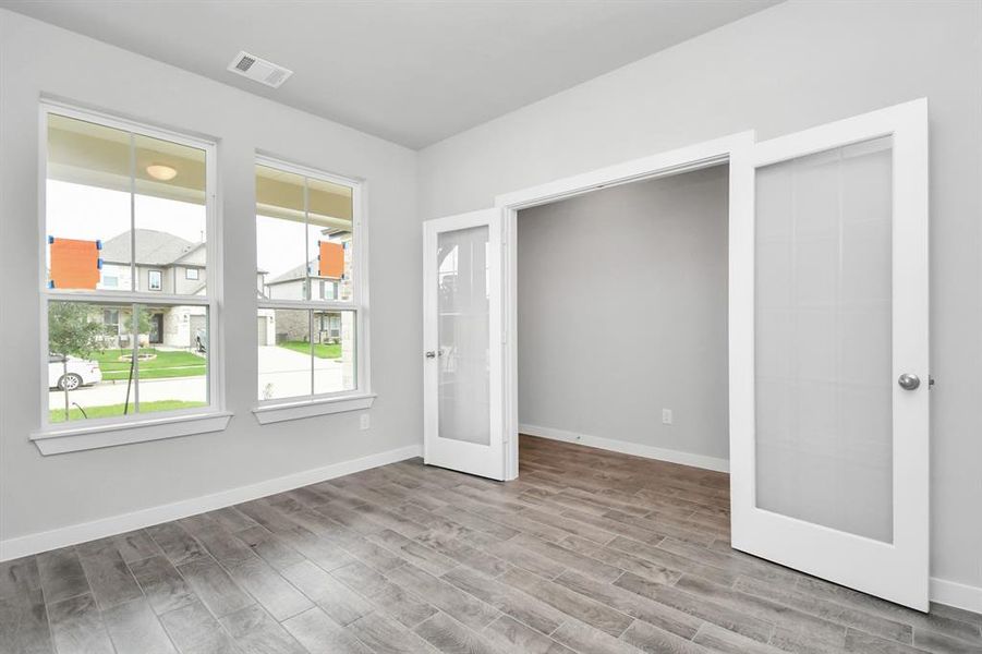 Perfect blend of sophistication and warmth in this home office, boasting elegant wood-look tile flooring and flooded with natural light from expansive windows and French doors. Sample photo of completed home with same plan. Actual colors and selections may vary.