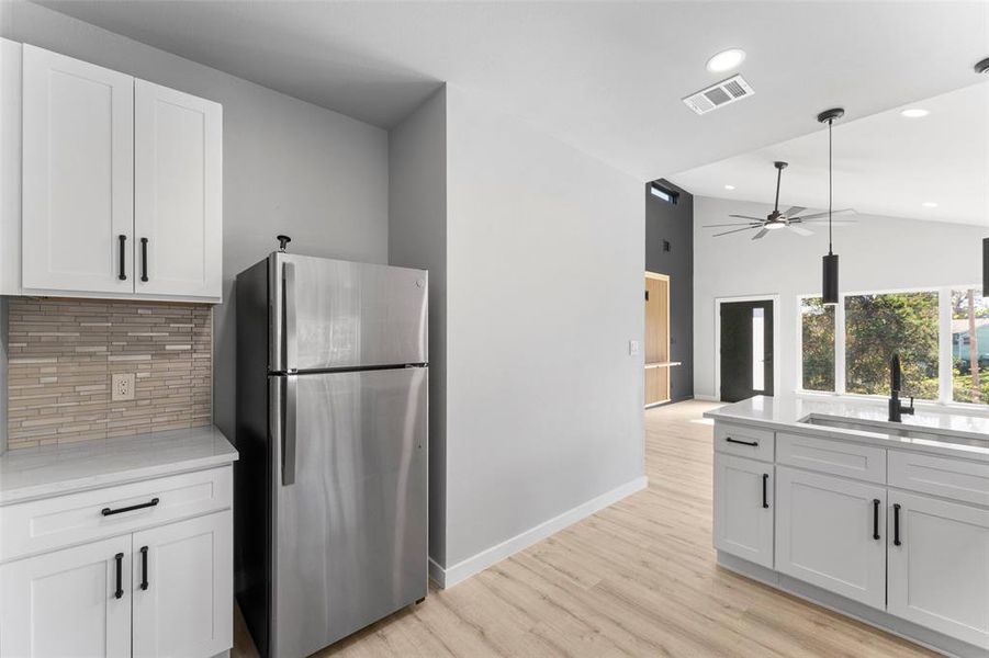 Kitchen featuring freestanding refrigerator, white cabinets, backsplash, light wood finished floors, and high vaulted ceiling