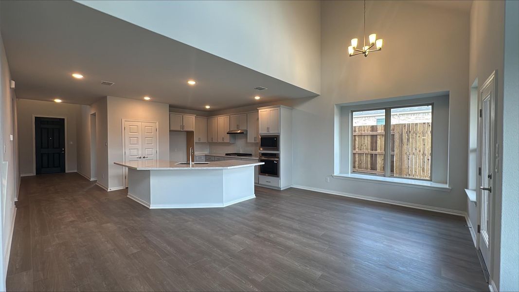 Kitchen with a high ceiling, dark wood-style flooring, a center island with sink, appliances with stainless steel finishes, and open floor plan Kitchen with a high ceiling, dark wood-style flooring, a center island with sink, appliances with stainless steel finishes, and open floor plan