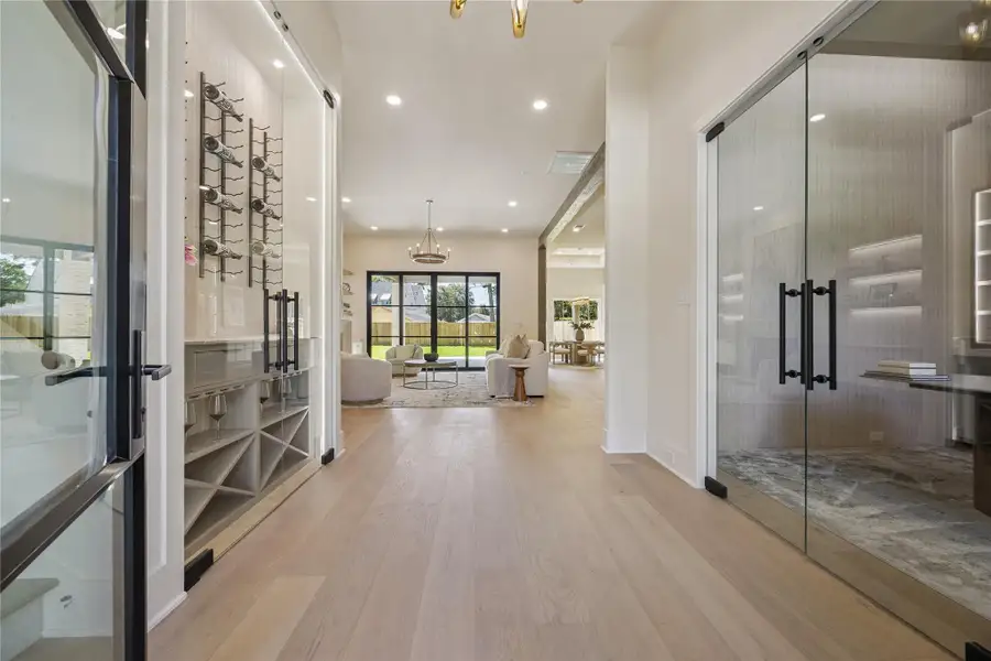ENTRY: A welcoming entry with soaring ceilings and white oak floors is flanked by a glass-enclosed wine display and private office, creating an unforgettable first impression.