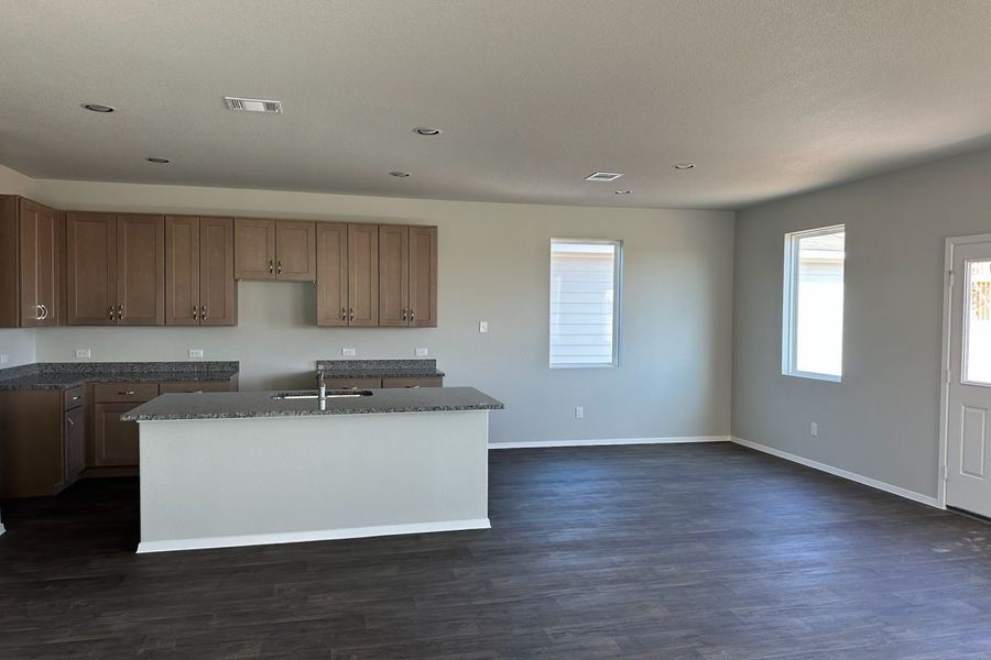 Image of home kitchen and dining room with light brown cabinets, center island, wood-look floors, and white walls with windows Image of home kitchen and dining room with light brown cabinets, center island, wood-look floors, and white walls with windows
