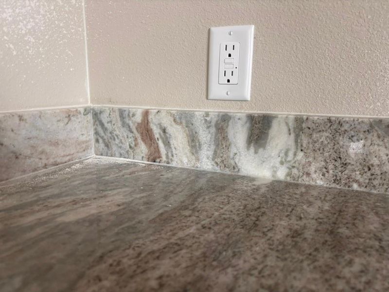 Granite-look countertop with a matching backsplash and a light-toned textured wall