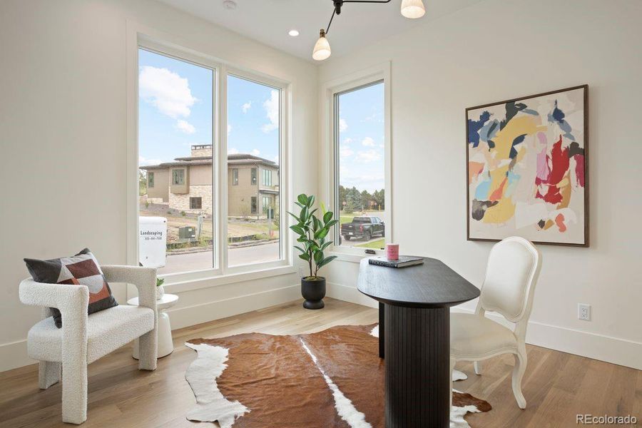 Main-floor office/study with large picture windows, warm wood flooring, and abundant natural light.
