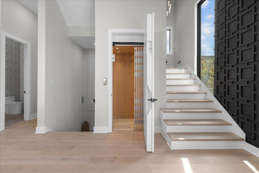 This modern home features a light-filled entryway with a sleek staircase and an elevator. A stylish black accent wall adds depth, while hardwood floors and neutral walls create a warm, inviting atmosphere. A bathroom is visible to the left, offering convenience. This modern home features a light-filled entryway with a sleek staircase and an elevator. A stylish black accent wall adds depth, while hardwood floors and neutral walls create a warm, inviting atmosphere. A bathroom is visible to the left, offering convenience.