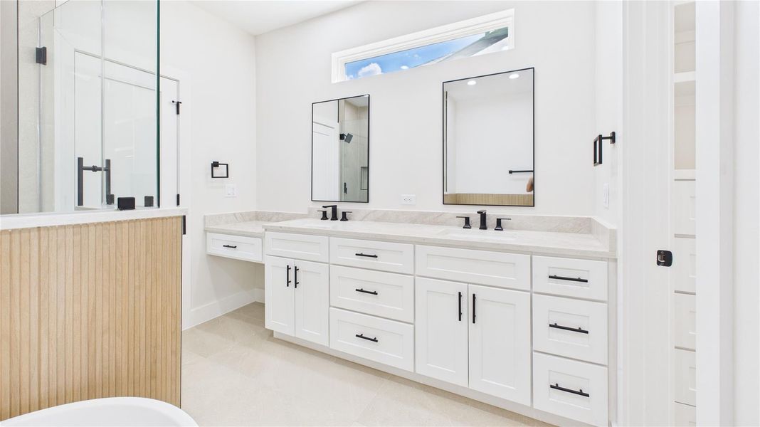 This bathroom features a modern design with a double vanity, sleek black fixtures, and ample storage. It has a glass-enclosed shower and a bright, airy atmosphere enhanced by a narrow window.