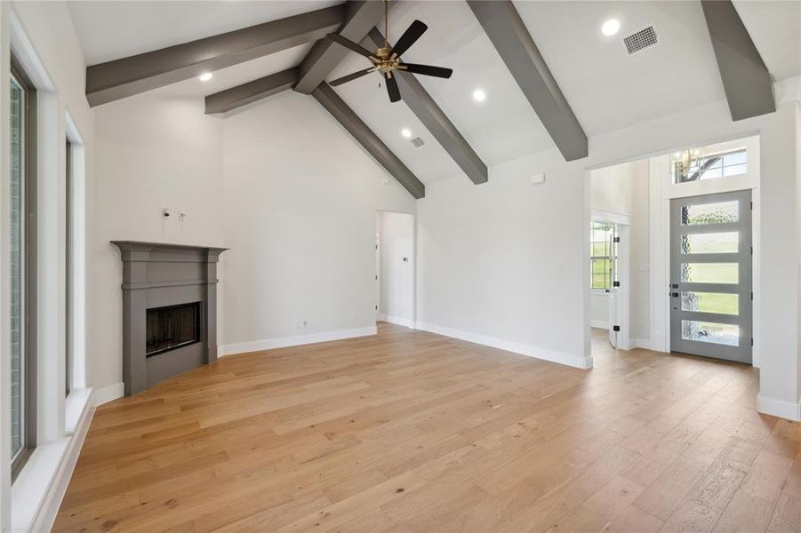 Unfurnished living room with light hardwood / wood-style floors, beam ceiling, ceiling fan with notable chandelier, and high vaulted ceiling