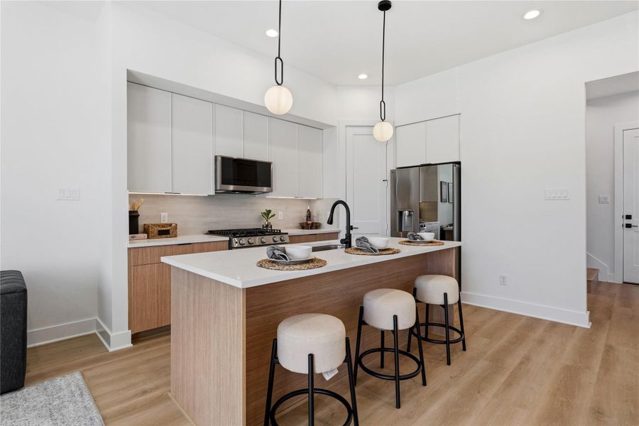 This space features two-tone cabinetry and a large stone-topped island. Minimalist pendants and integrated appliances highlight the clean, functional geometry.
