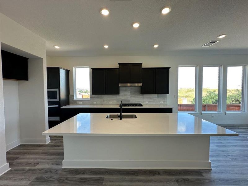 Kitchen featuring a large central island with a solid surface countertop, dark cabinetry, and integrated stainless steel appliances Kitchen featuring a large central island with a solid surface countertop, dark cabinetry, and integrated stainless steel appliances
