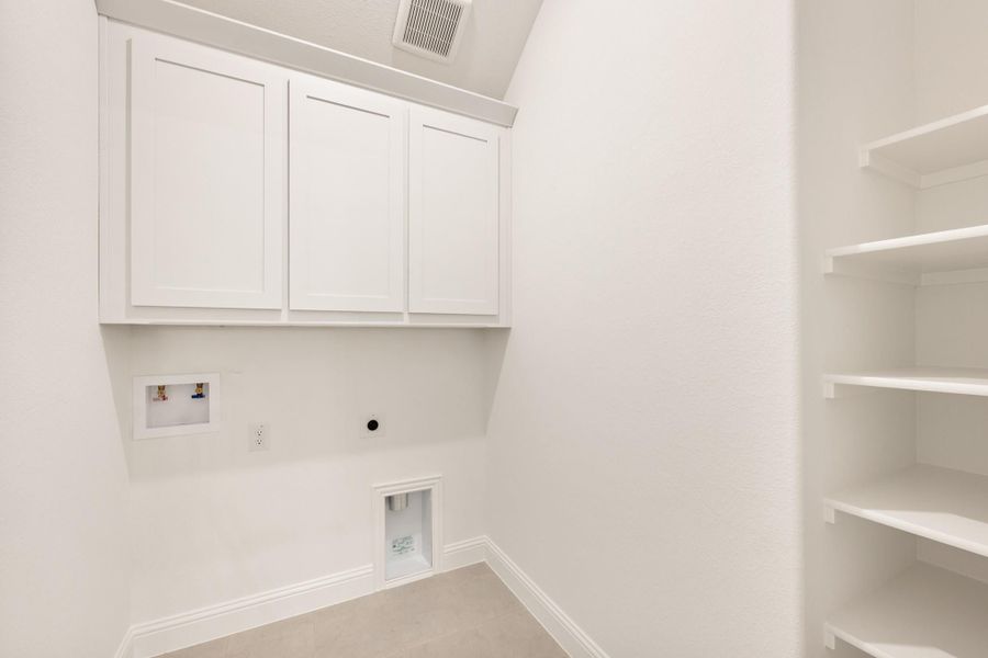 Laundry room with white upper cabinets, open shelving, and washer and dryer hookups on white walls.