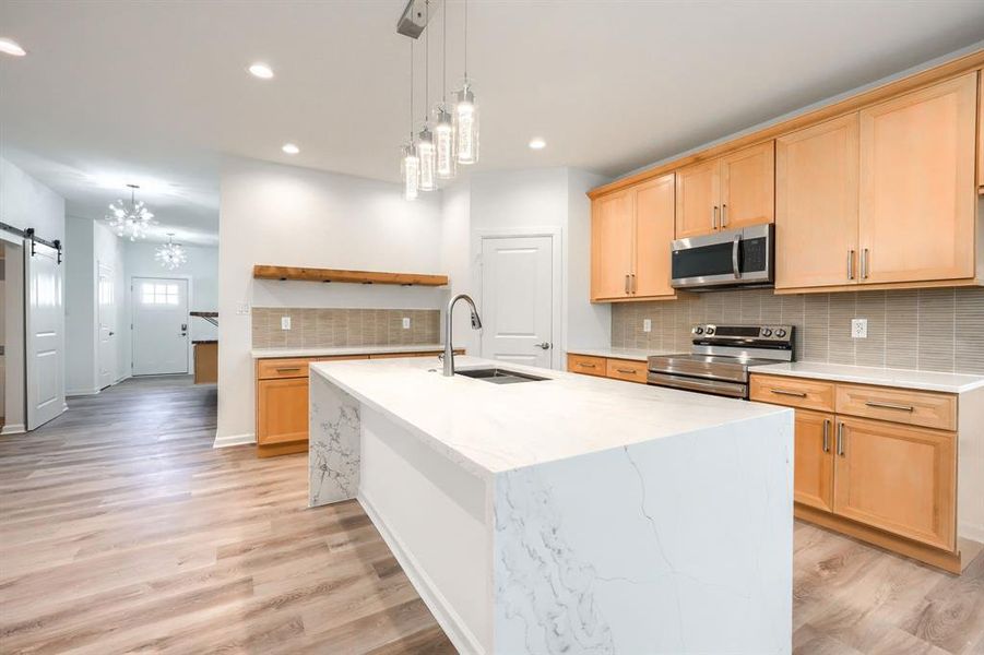 Kitchen featuring decorative backsplash, a barn door, light stone counters, a chandelier, and stainless steel appliances