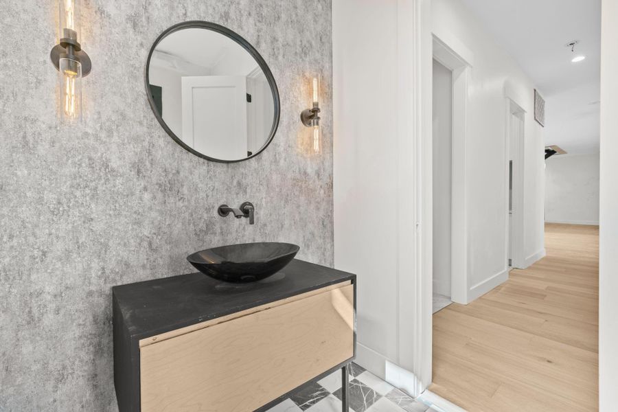 This sleek wall mounted sink anchors the space with clean, contemporary lines , freeing up floor area for an airy open feel. The polished chrome and brushed nickel faucet adds a touch of understated elegance with a graceful curve that complements the minimalist aesthetic. Beneath it , stylish floating vanity overs clever storage.