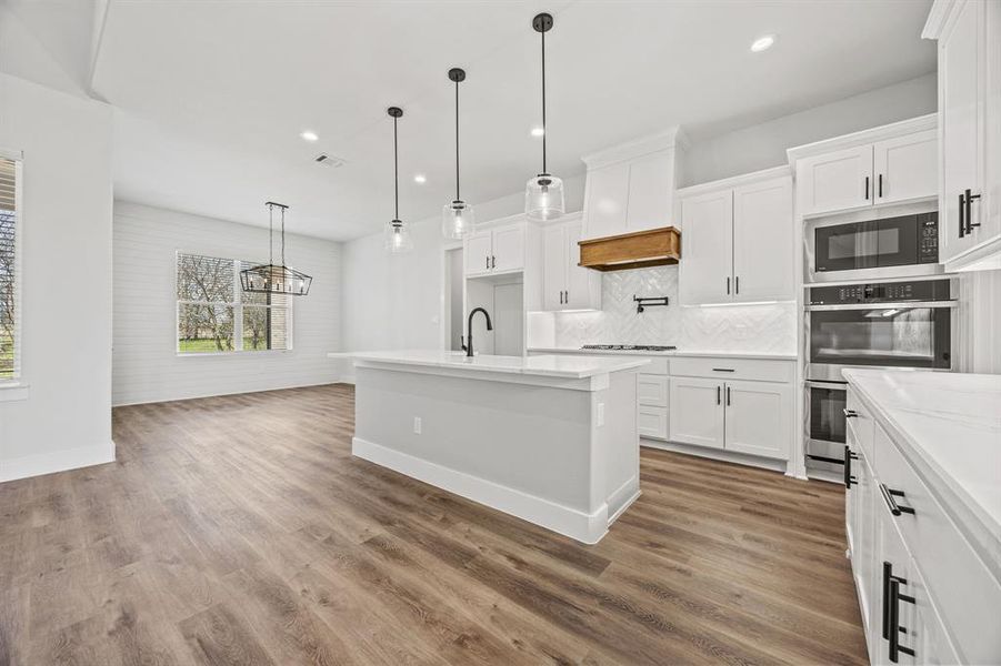 Kitchen with light countertops, backsplash, white cabinetry, wood finished floors, and recessed lighting Kitchen with light countertops, backsplash, white cabinetry, wood finished floors, and recessed lighting