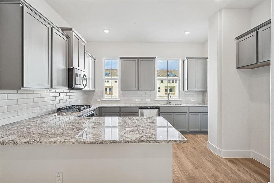 Kitchen with gray cabinetry, light wood-type flooring, light stone countertops, backsplash, and recessed lighting