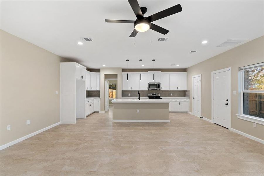 Kitchen featuring pendant lighting, ceiling fan, an island with sink, appliances with stainless steel finishes, and white cabinetry