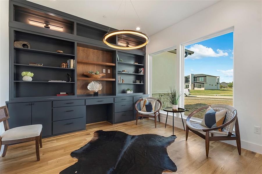 Built-in dark cabinetry with integrated desktop, wood-finish shelving, and overhead lighting Built-in dark cabinetry with integrated desktop, wood-finish shelving, and overhead lighting