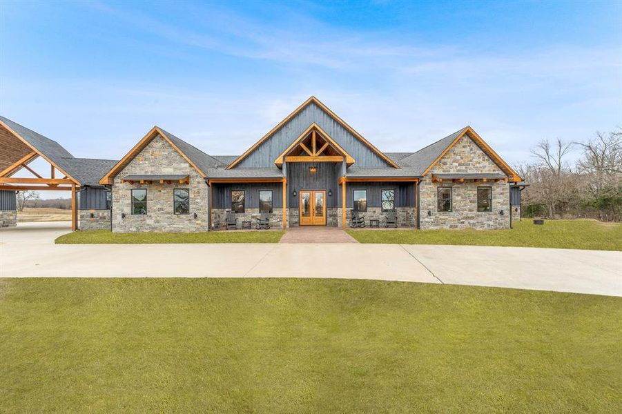 View of front of house with stone siding, a front yard, and a porch