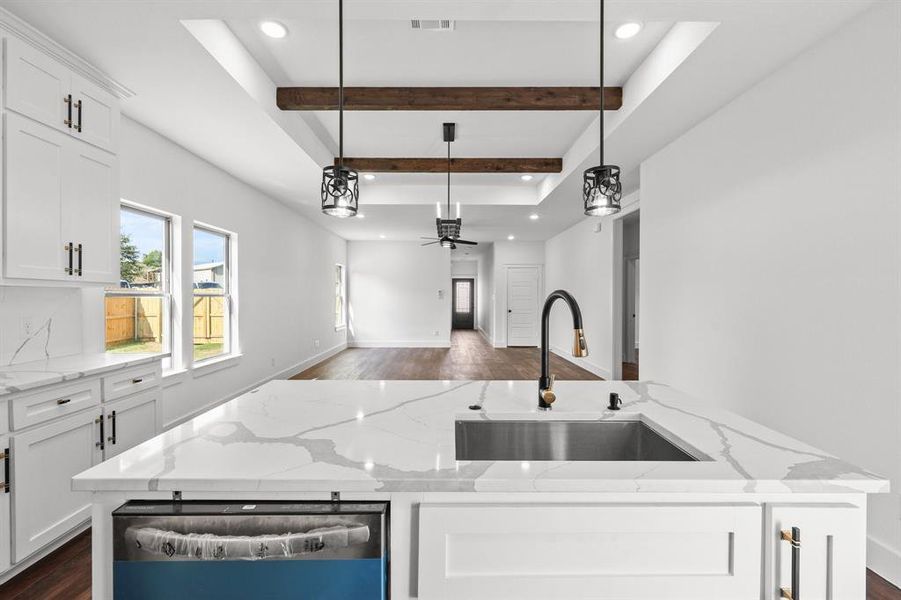 Kitchen featuring decorative light fixtures, light stone countertops, a center island with sink, ceiling fan, and white cabinets