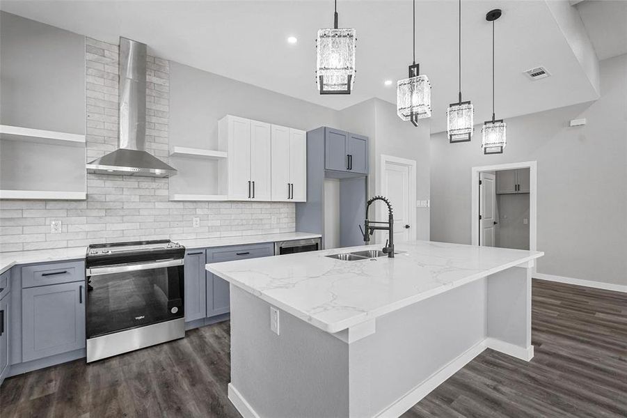 Kitchen featuring light stone counters, sink, an island with sink, stainless steel stove, and wall chimney range hood