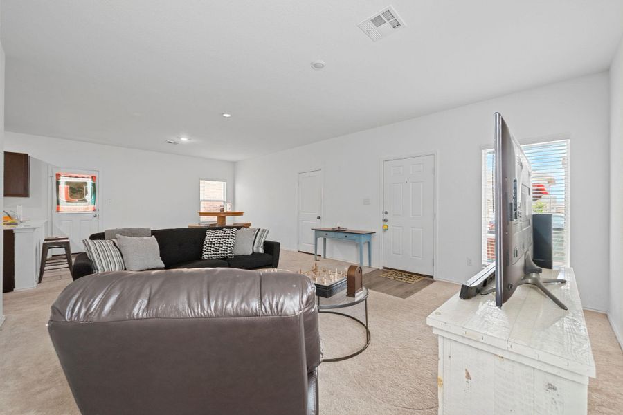 Open-concept living area featuring light-colored carpet flooring and white painted walls