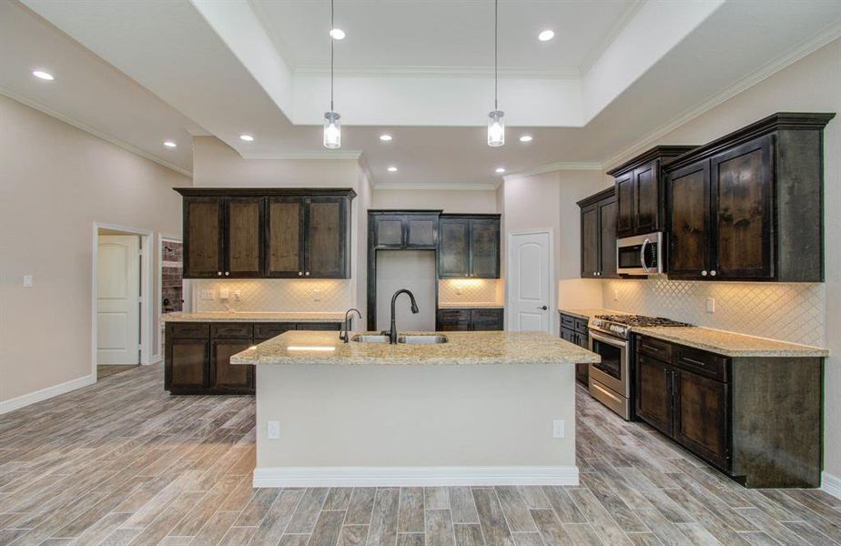 This is a spacious, modern kitchen featuring dark wood cabinetry, granite countertops, stainless steel appliances, and a central island. The room has recessed lighting and wood-look tile flooring, creating a contemporary and elegant atmosphere.