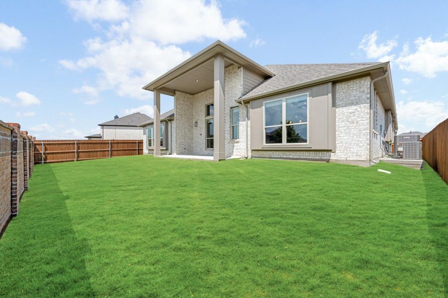 Backyard of a single-story home with stone exterior, covered patio, green lawn, and wood privacy fence. Backyard of a single-story home with stone exterior, covered patio, green lawn, and wood privacy fence.