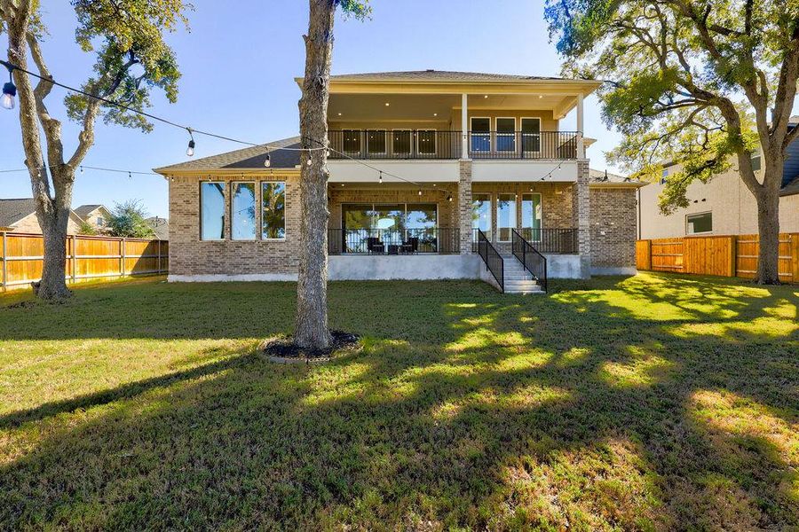 Rear view of house with a balcony, a patio area, brick siding, and a fenced backyard