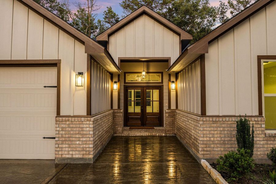 The home entrance with a warm and inviting design.  The well-lit pathway leads to a grand double door, flanked by stylish exterior lights, underlining the home's elegance and curb appeal.